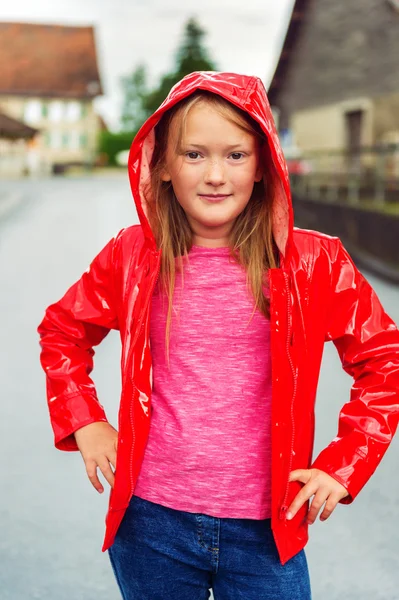 Svislý venkovní portrét roztomilá holčička 8-9 let na zamračený den, nosí zářivě červenou pláštěnku — Stock fotografie