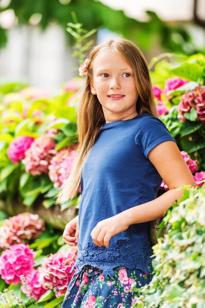 Outdoor vertical portrait of a cute little girl of 9 years old in summer garden, leaning on a fence, wearing blue tee shirt — Stock Photo, Image