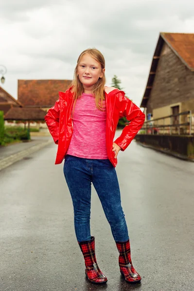 Parlak kırmızı yağmur ceket giyen sevimli küçük bir kız bulutlu bir günde, 8-9 yaşında dikey açık portresi — Stok fotoğraf