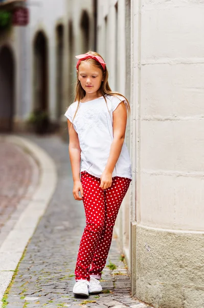 Outdoor fashion portrait of a ute little girl of 8-9 years old walking down the street, wearing polkadot trousers and white tee shirt — Stock Photo, Image