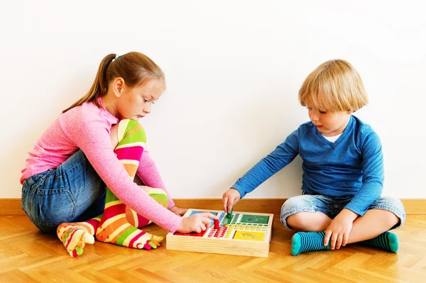 Two cute kids, little brother and his big sister playing board games at home, wearing funny socks — Stock Photo, Image