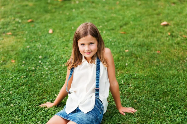 Portrait of a cute little girl 7-8 year old in the park, sitting on grass — Stock Photo, Image