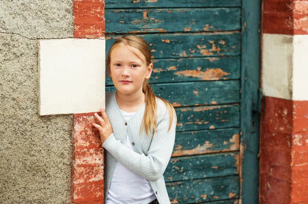 Außenporträt eines netten kleinen Mädchens im Alter von 8-9 Jahren, das eine graue Strickjacke trägt und neben einer alten grünen Tür steht — Stockfoto