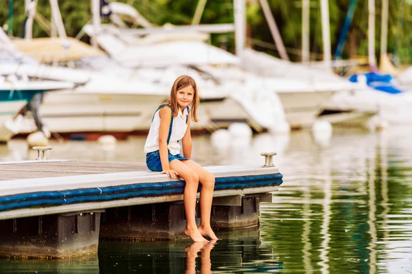 Niedliches kleines Mädchen, das sich am See ausruht, auf einem Steg sitzt — Stockfoto