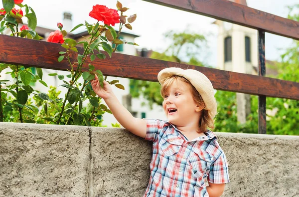 Entzückender kleiner Gärtnerjunge, der draußen mit Rosen spielt — Stockfoto