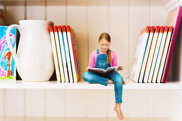 Menina sentada na estante e lendo interessante livro de história. Educação e escola, estudo e literatura . — Fotografia de Stock