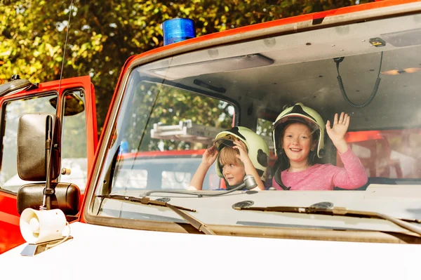 Two cute kids playing in fire truck, pretending to be firefighters, open doors day at fire station. Future profession for children. Educational programme for schoolkids — Stock Photo, Image