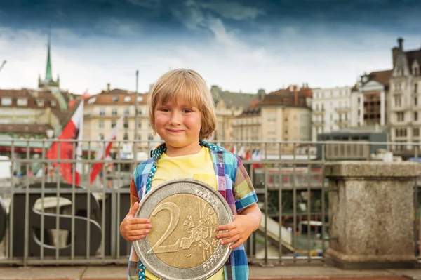 Außenporträt eines niedlichen kleinen Jungen in einer Stadt mit einer riesigen 2-Euro-Münze — Stockfoto