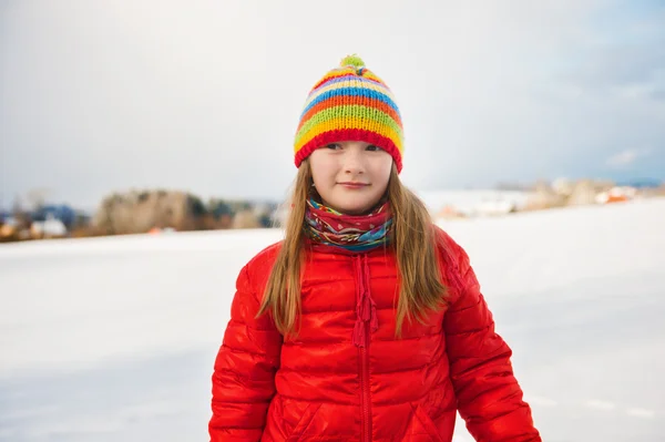 Little girl wearing red jacket and colorful hat, playing with snow in winter time — Stock Photo, Image