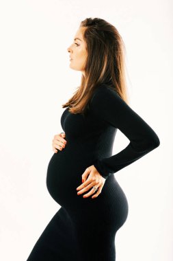 Beyaz arka planda poz veren, siyah kaplumbağa yakalı, harika bir kadının hamile portresi. 