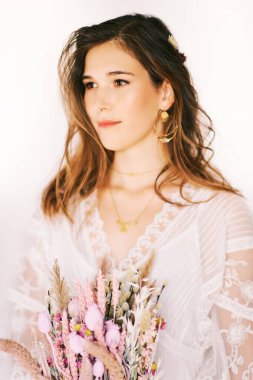 Boho tarzı elbise giyen güzel bir kadının moda portresi, elinde kuru çiçekler, beyaz arka planda hippi tarzı poz veren bir model.