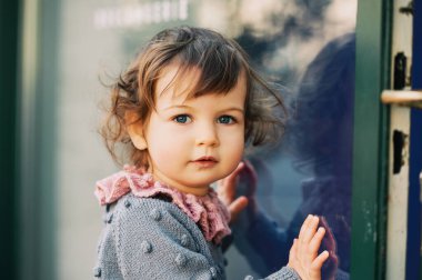 Kıvırcık saçlı, mavi gözlü, kazak giyen sevimli bir kızın portresi.
