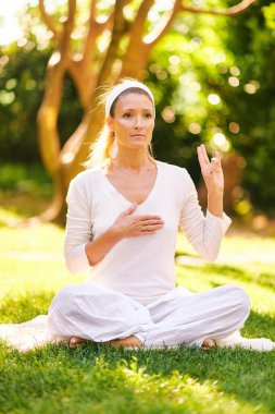 Güzel olgun bir kadın yeşil güneşli bahçede meditasyon yapıyor, sağlıklı bir yaşam tarzı var.
