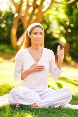 Güzel olgun bir kadın yeşil güneşli bahçede meditasyon yapıyor, sağlıklı bir yaşam tarzı var.