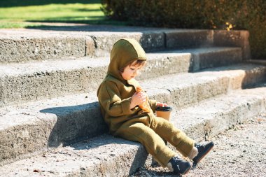 Sabahın erken saatlerinde ayçöreği yiyip kahve fincanından içen, merdivenlerde oturan komik küçük çocuk.