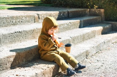 Sabahın erken saatlerinde ayçöreği yiyip kahve fincanından içen, merdivenlerde oturan komik küçük çocuk.