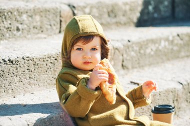 Sabahın erken saatlerinde ayçöreği yiyip kahve fincanından içen, merdivenlerde oturan komik küçük çocuk.