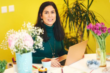 Renkli ofiste çalışan orta yaşlı güzel bir kadın taşınabilir dizüstü bilgisayar kullanıyor.