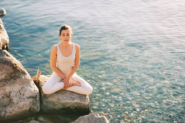 Beautiful spiritual woman meditating by the lake, wearing beige clothes