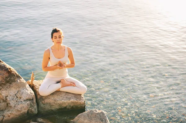 Beautiful spiritual woman meditating by the lake, wearing beige clothes