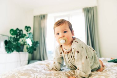 Güzel bir bebeğin portresi. 1 yaşında, mankenli bir kız, ailesinin yatağında sürünüyor.