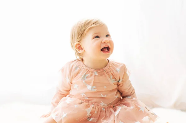 かわいいです若いです1歳の女の子 ピンクのドレスを着て 窓の横に座って — ストック写真