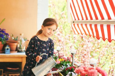 Cute little girl watering plants on small cozy balcony