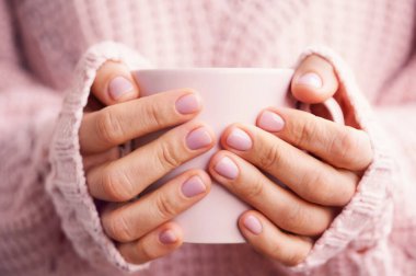 Cup of coffee or tea in woman's hands with soft pink manicure