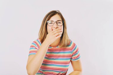 Gökkuşağı tişörtü ve gözlük takan genç mutlu bir mankenin stüdyo portresi, gülen genç kız eli ile ağzını kapatıyor.