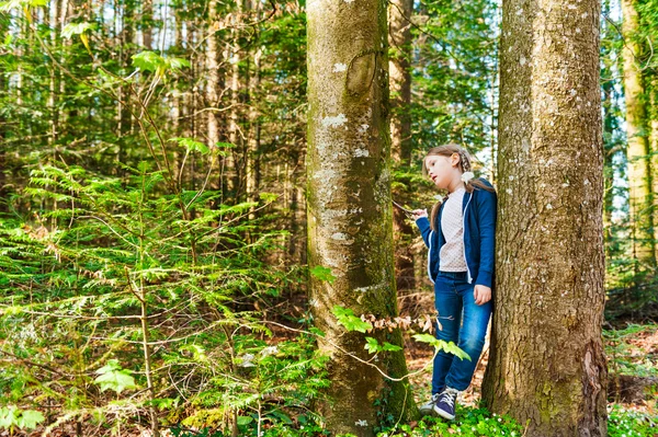 Söt liten flicka spela mellan träd i en skog på en fin solig dag — Stockfoto