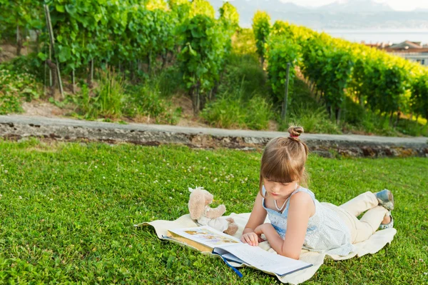 Portrait of adorable little girl resting outdoors and reading a book on a nice summer evening — Stock Photo, Image