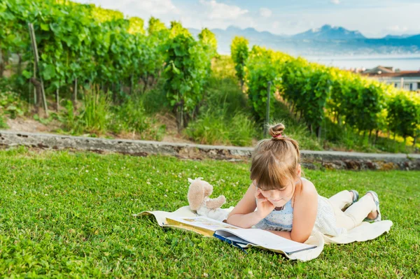 Portrait of adorable little girl resting outdoors and reading a book on a nice summer evening — Stock Photo, Image