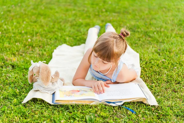 Ritratto di adorabile bambina che riposa all'aperto e legge un libro in una bella serata estiva — Foto Stock