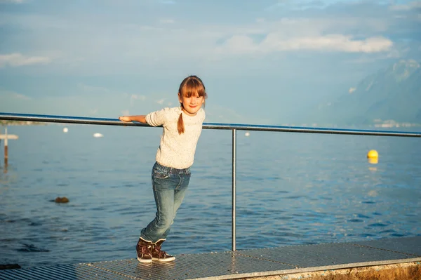 Sunset portrait of a cute little girl next to beautiful lake, wearing beige knitted pullover and jeans — Stock Photo, Image