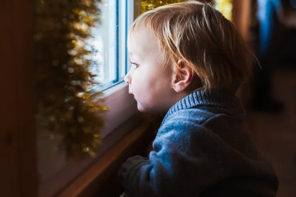 Bonito menino da criança olhando para a janela na época do Natal — Fotografia de Stock