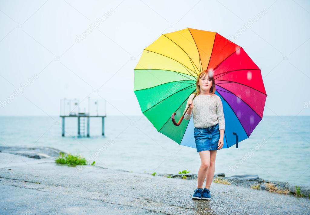 Outdoor portrait of a cute little girl with colorful umbrella under the rain