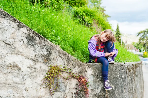 Retrato ao ar livre de uma menina bonito, sentado em uma parede de pedra, início da primavera — Fotografia de Stock