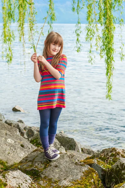 Utendørs portrett av en søt liten jente på en solrik dag, mens hun leker ved siden av en vakker innsjø – stockfoto