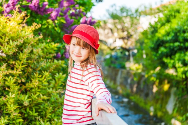 Utomhus porträtt av en vacker liten flicka i en röd hatt, en fin solig dag — Stockfoto