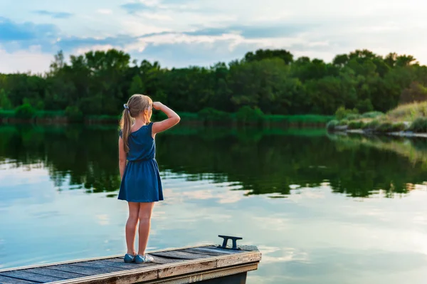 Außenporträt eines niedlichen kleinen Mädchens, das auf einem Pier steht und abends auf eine wunderschöne Lagune blickt — Stockfoto