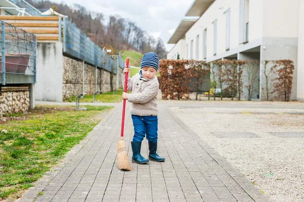 Menino bonito varrendo o quintal em um dia de primavera cedo — Fotografia de Stock