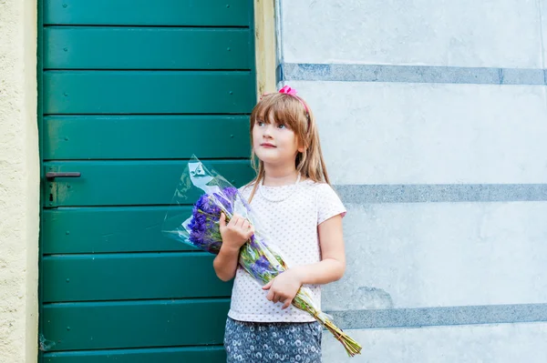 Entzückendes kleines Mädchen mit einem Strauß violetter Blumen — Stockfoto