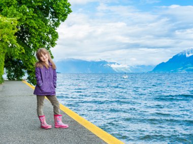 Açık yağmur ceket ve çizmeler giyen sevimli küçük bir kız portresi
