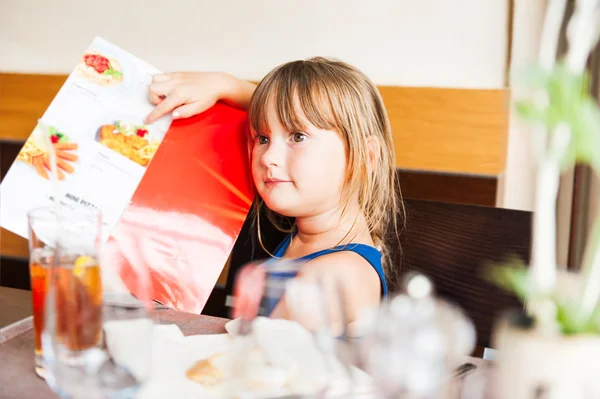 Cute little giel choosing her meal in a kid's menu in a restaurant — Stock Photo, Image