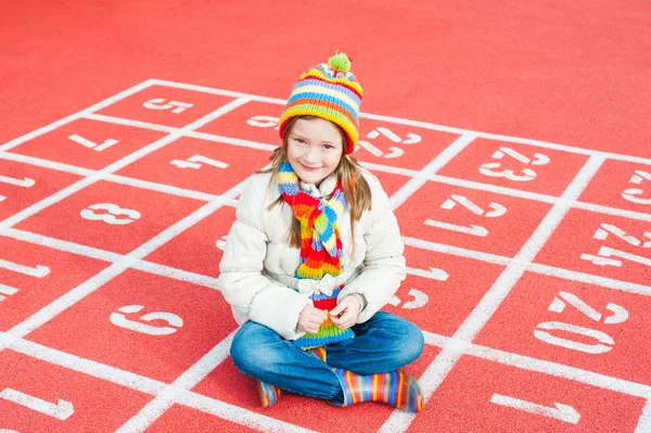 Retrato ao ar livre de uma menina bonita usando jaqueta e chapéu colorido e cachecol — Fotografia de Stock