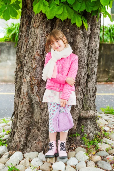 Retrato al aire libre de una linda niña, con chaqueta rosa y botas, de pie junto a un hermoso castaño —  Fotos de Stock