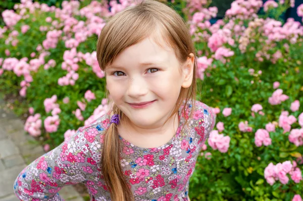 Pretty little girl outdoor portrait with pink roses on background — Stock Photo, Image