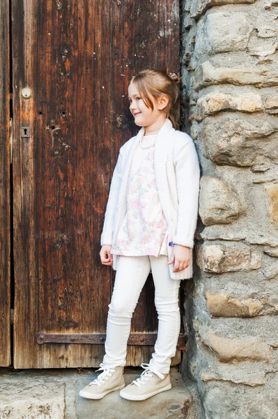 Cute little girl posing outdoors against wooden door, wearing white clothes — Stock Photo, Image
