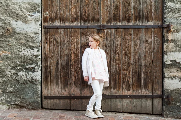 Carino bambina posa all'aperto contro la porta di legno, indossando vestiti bianchi — Foto Stock