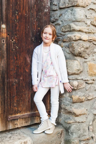 Menina bonito posando ao ar livre contra a porta de madeira, vestindo roupas brancas — Fotografia de Stock